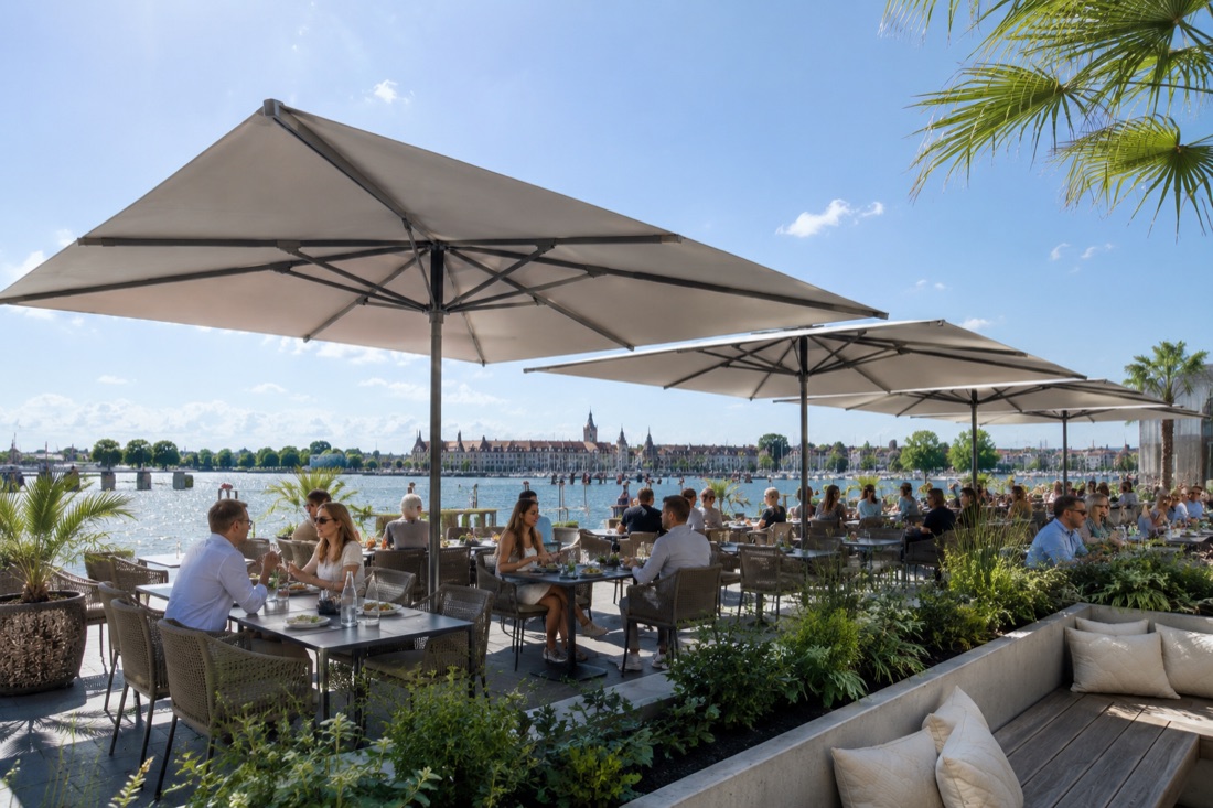 Große Sonnenschirme über einer belebten Restaurantterrasse am Wasser bei Tageslicht