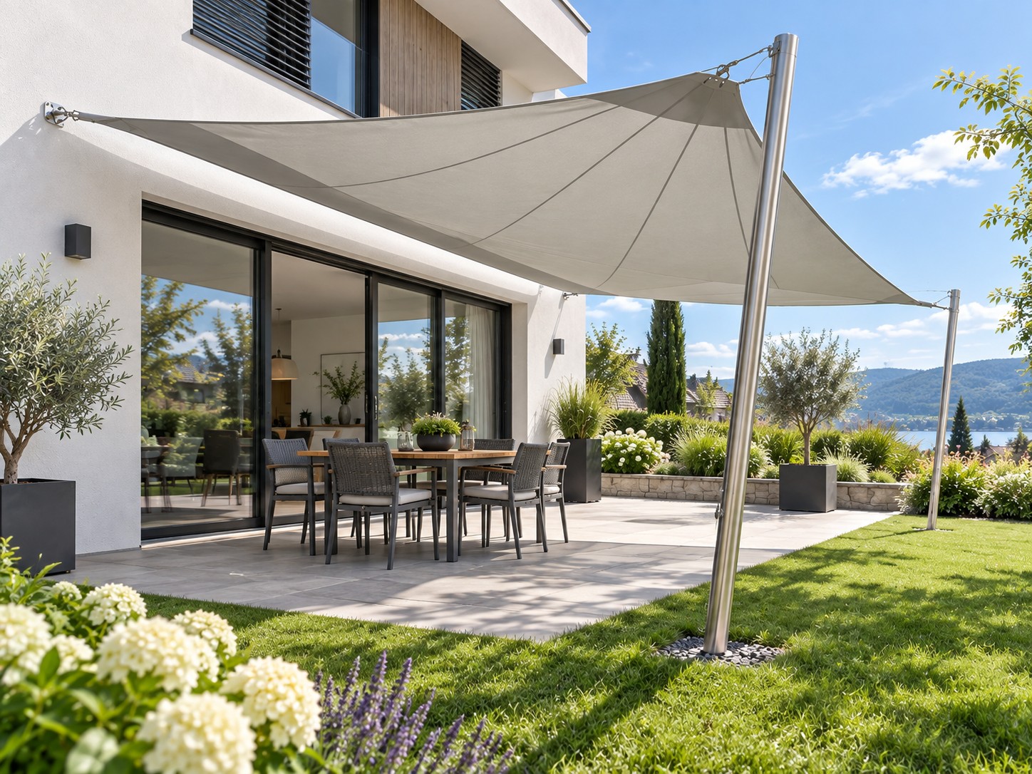 Taupegraues gespanntes Sonnensegel mit sichtbaren Seilbefestigungen zwischen Hauswand und Edelstahlmasten im Garten
